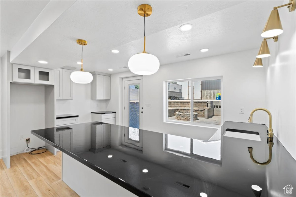Kitchen featuring light wood-style floors, white cabinetry, recessed lighting, dark countertops, and glass insert cabinets