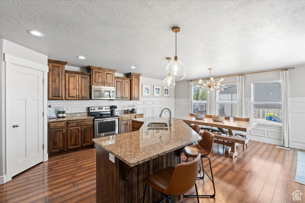 Kitchen featuring appliances with stainless steel finishes, a sink, dark wood-style flooring, a textured ceiling, and a decorative wall