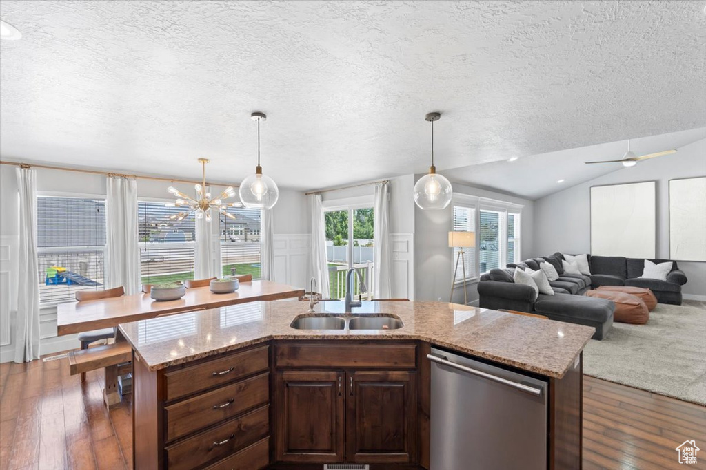 Kitchen with dishwasher, a sink, dark wood-style floors, a textured ceiling, and a kitchen island with sink