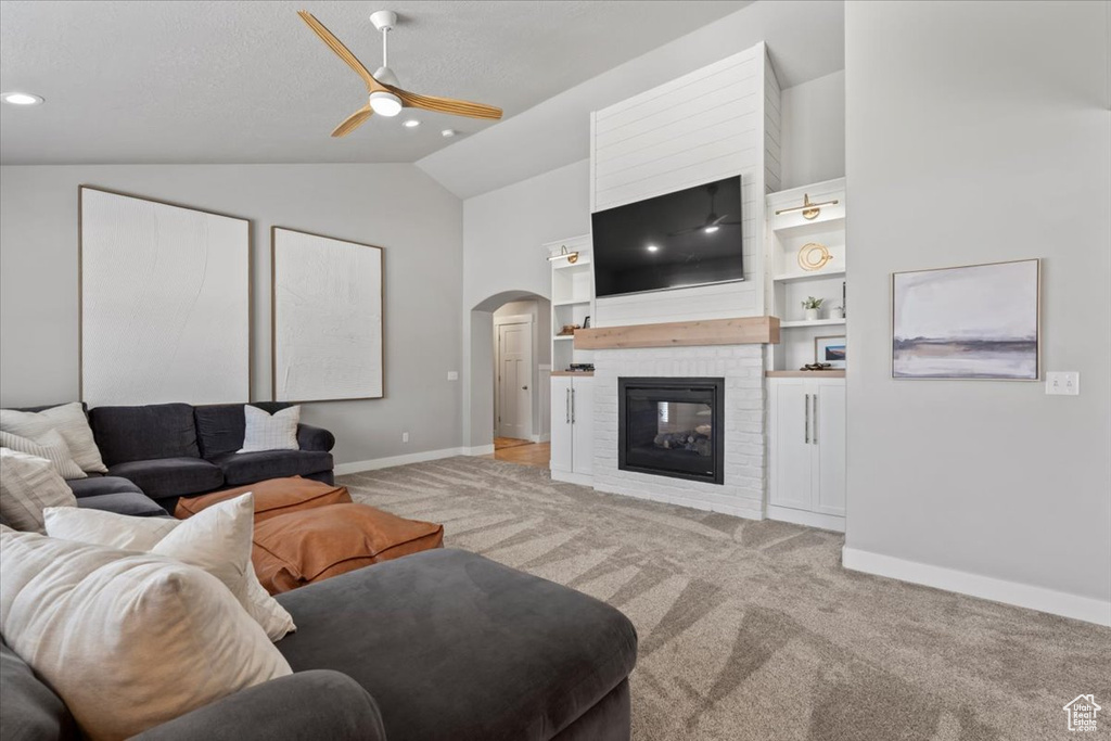 Living room with arched walkways, ceiling fan, light colored carpet, vaulted ceiling, and baseboards