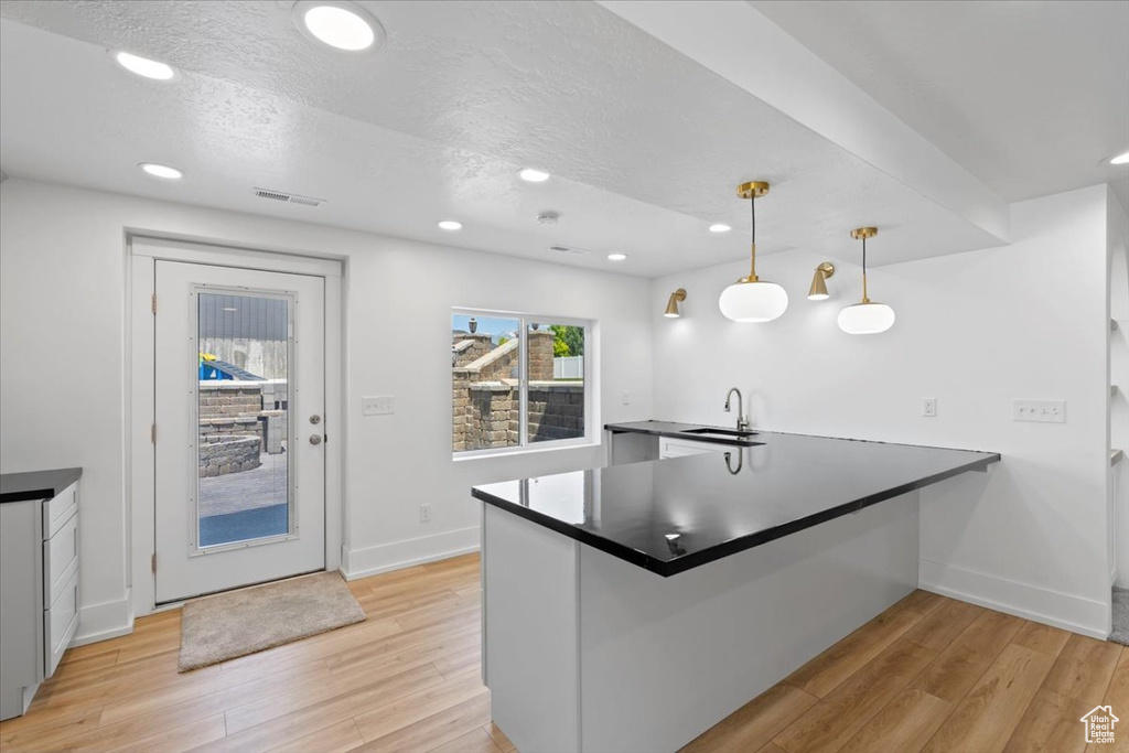 Kitchen featuring a sink, a peninsula, light wood finished floors, dark countertops, and recessed lighting