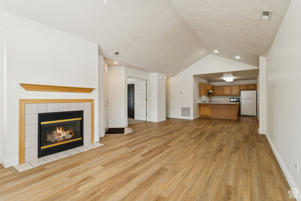 Unfurnished living room with a tile fireplace, light wood finished floors, vaulted ceiling, baseboards, and recessed lighting