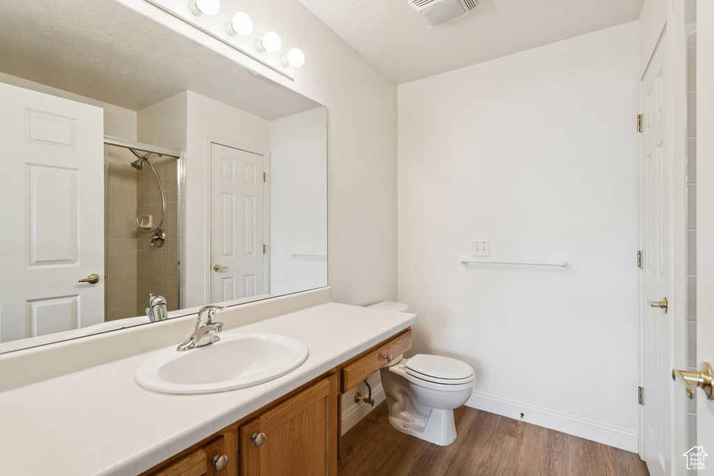 Bathroom with vanity, wood finished floors, toilet, a tile shower, and baseboards