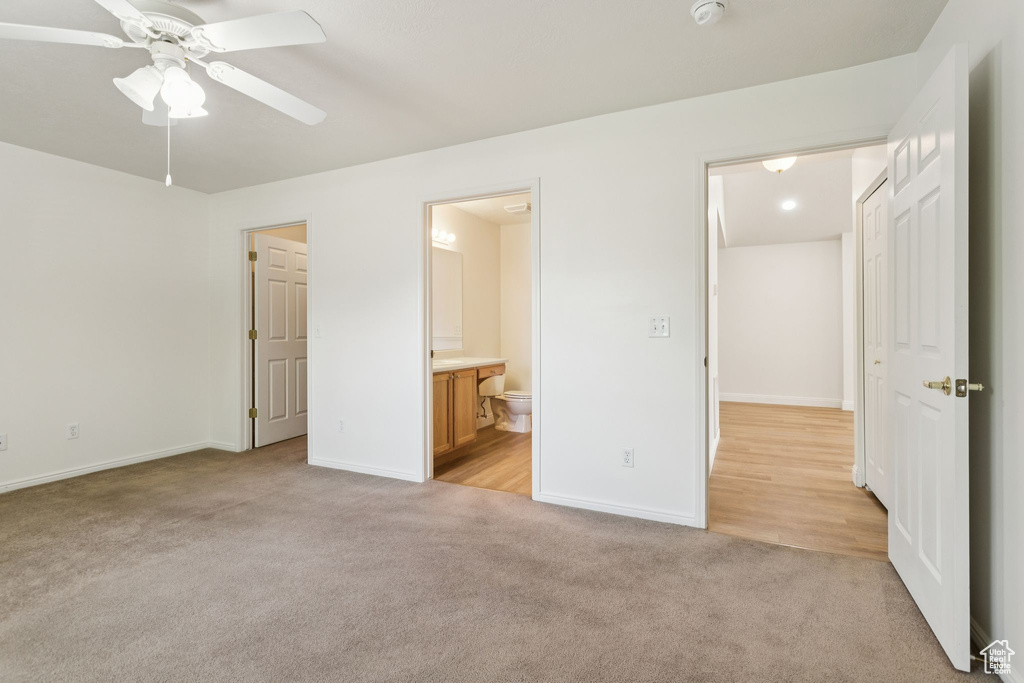 Unfurnished bedroom featuring light carpet, baseboards, ensuite bathroom, and a ceiling fan