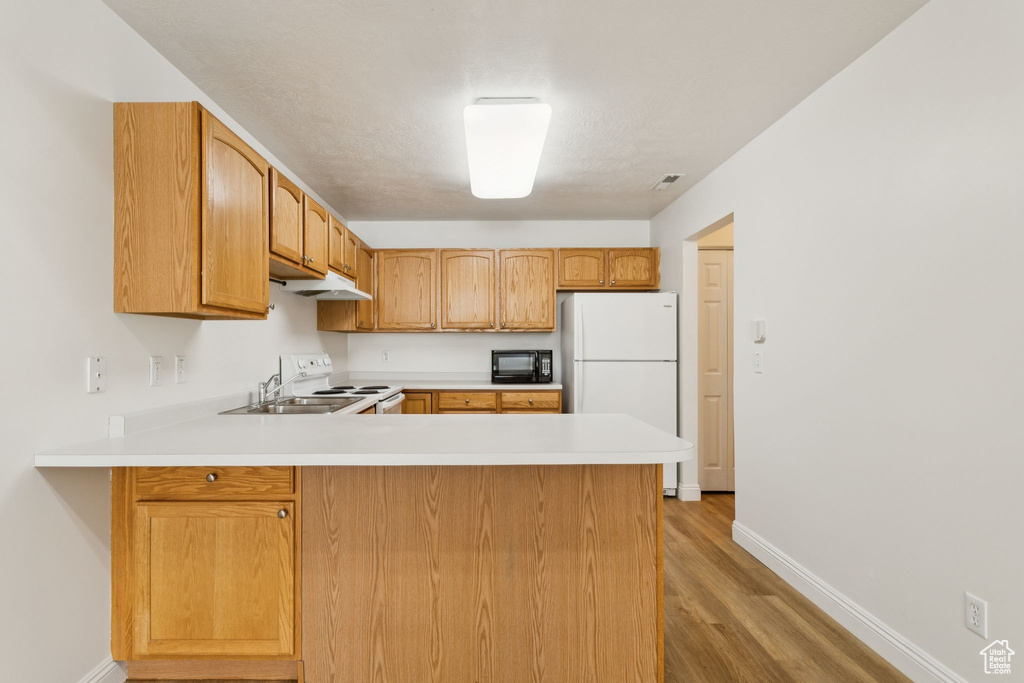 Kitchen featuring white appliances, a peninsula, light wood finished floors, and light countertops