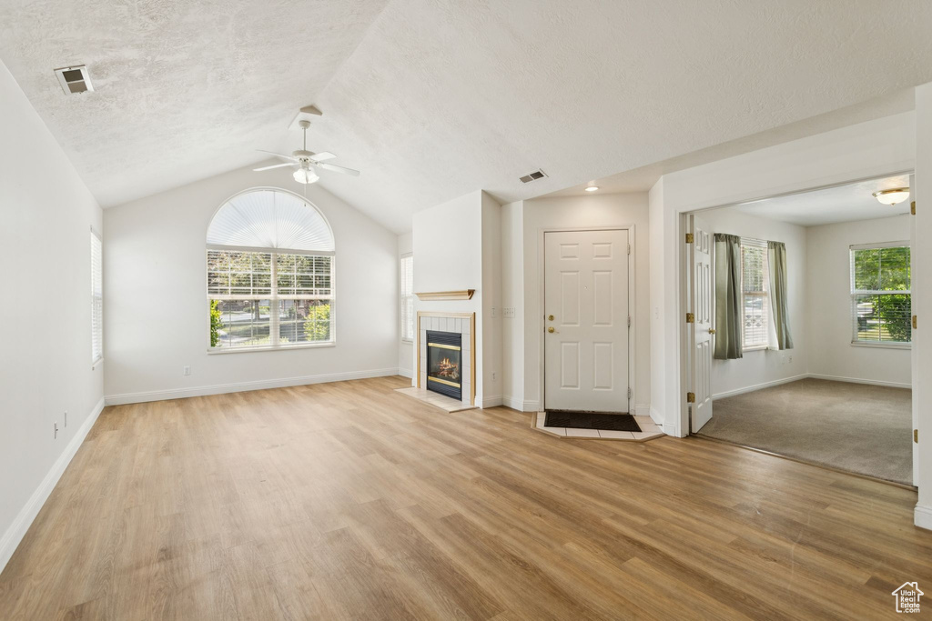Unfurnished living room featuring a ceiling fan, light wood-style floors, lofted ceiling, a fireplace, and baseboards