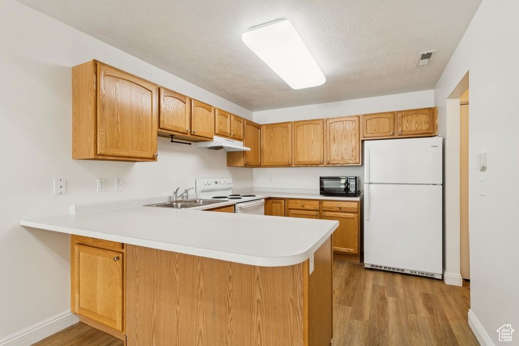 Kitchen featuring white appliances, under cabinet range hood, a sink, light countertops, and light wood-style floors