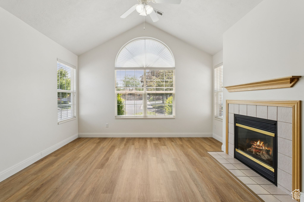 Unfurnished living room featuring light wood-type flooring, a tile fireplace, ceiling fan, lofted ceiling, and baseboards