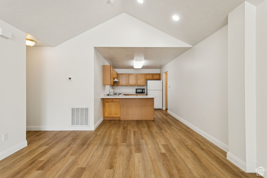 Kitchen featuring freestanding refrigerator, a peninsula, open floor plan, light countertops, and light wood-style floors