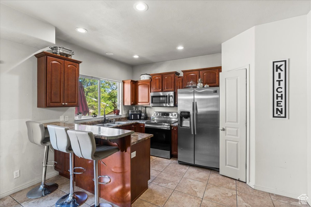 Kitchen with appliances with stainless steel finishes, a sink, a peninsula, a breakfast bar area, and recessed lighting