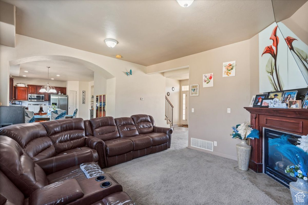 Living room with arched walkways, light colored carpet, a glass covered fireplace, a chandelier, and stairway