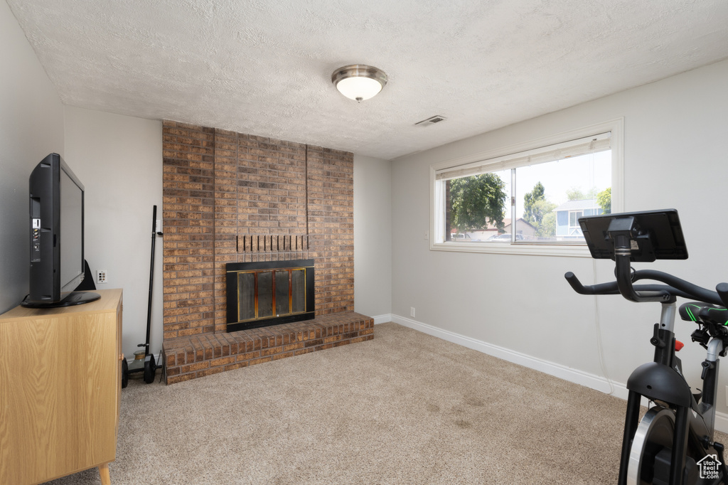 Exercise area with carpet, a fireplace, a textured ceiling, and baseboards