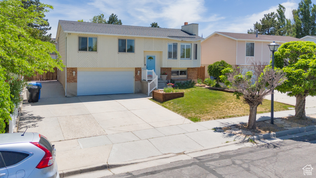 Bi-level home with brick siding, a garage, driveway, a front yard, and roof with shingles