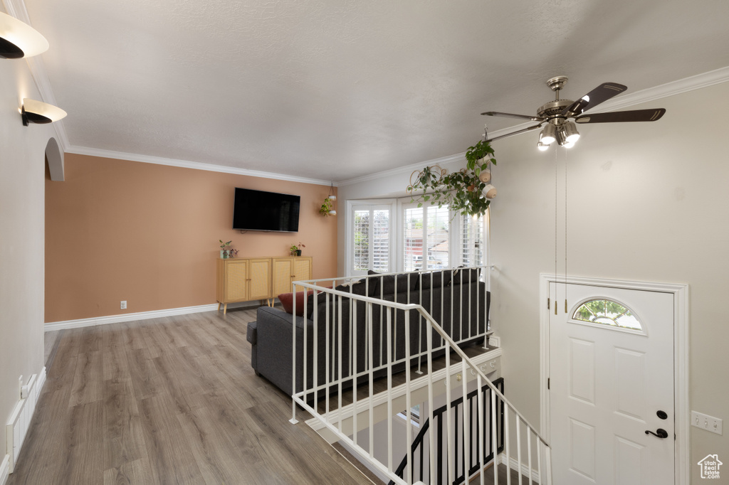 Foyer featuring a ceiling fan, wood finished floors, ornamental molding, arched walkways, and baseboards