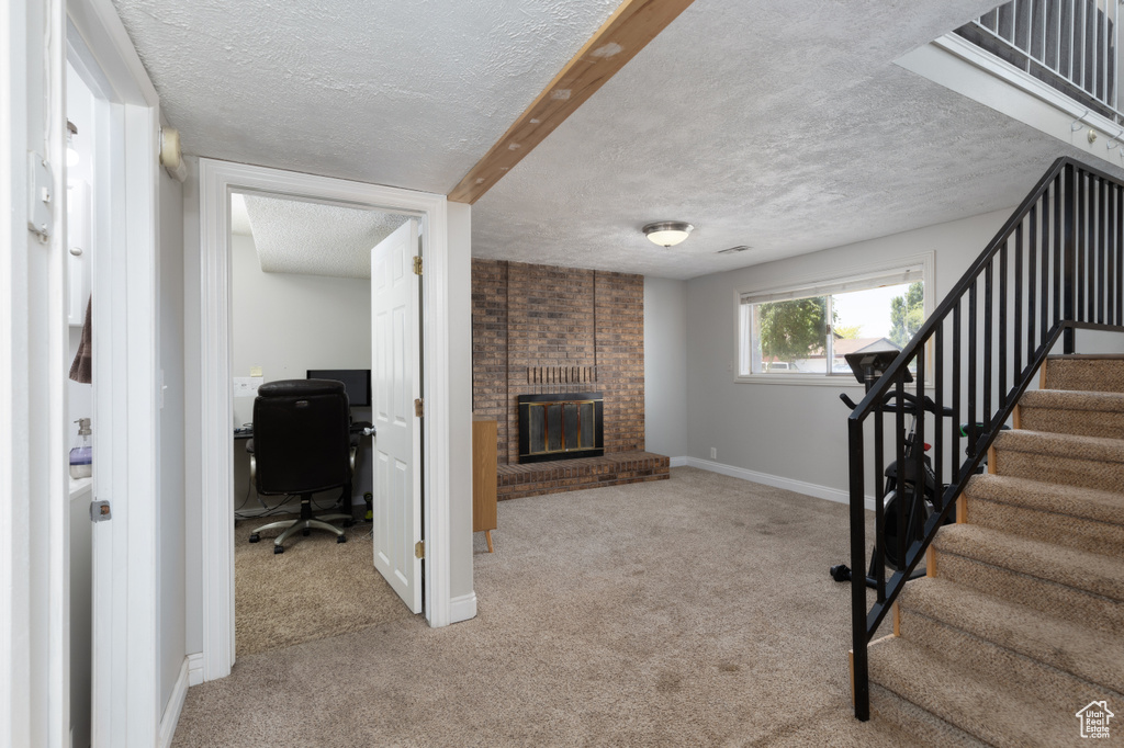 Unfurnished living room with a textured ceiling, carpet flooring, a fireplace, stairway, and an office area