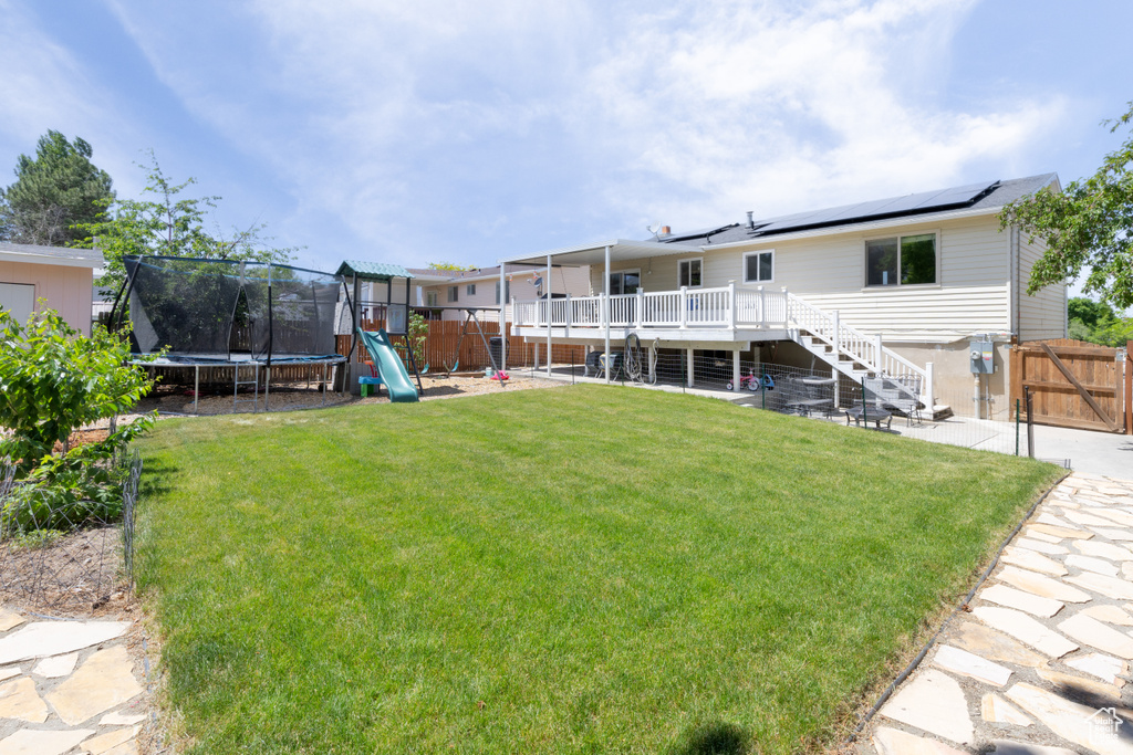 View of yard featuring a trampoline, stairs, a deck, a playground, and a gate