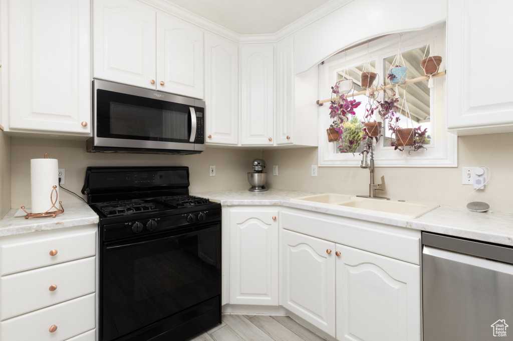 Kitchen featuring appliances with stainless steel finishes, white cabinetry, a sink, and light countertops