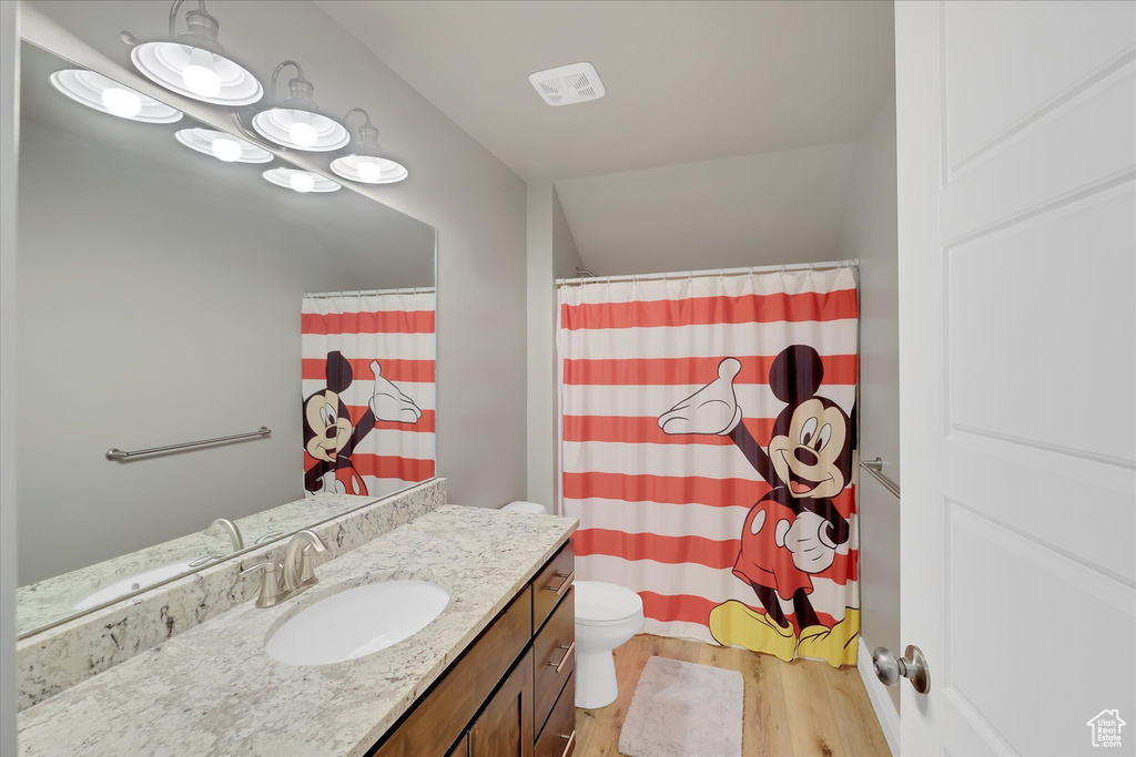 Bathroom with wood finished floors, vanity, toilet, curtained shower, and lofted ceiling
