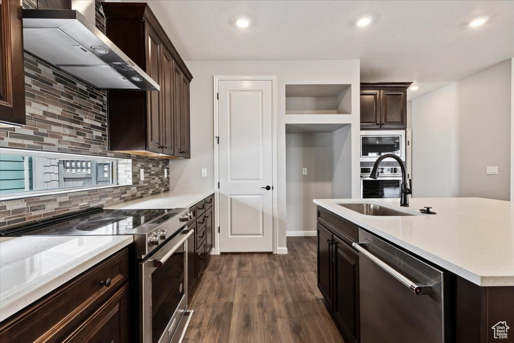 Kitchen featuring appliances with stainless steel finishes, wall chimney exhaust hood, a sink, dark wood-style floors, and decorative backsplash