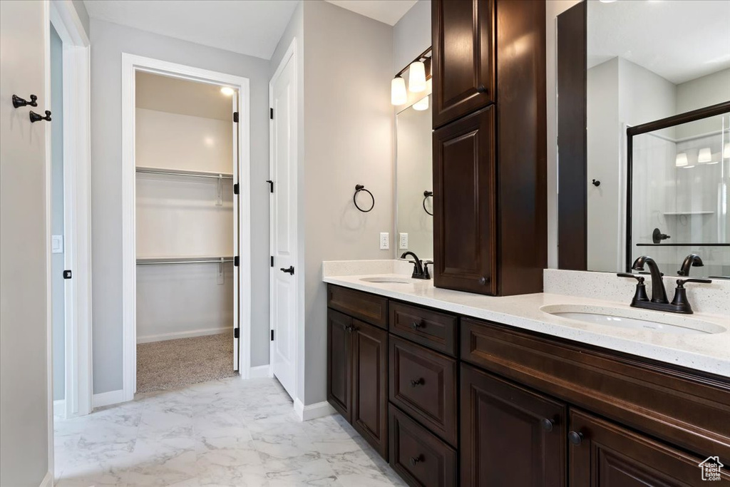 Full bath with marble finish flooring, double vanity, a stall shower, a spacious closet, and baseboards