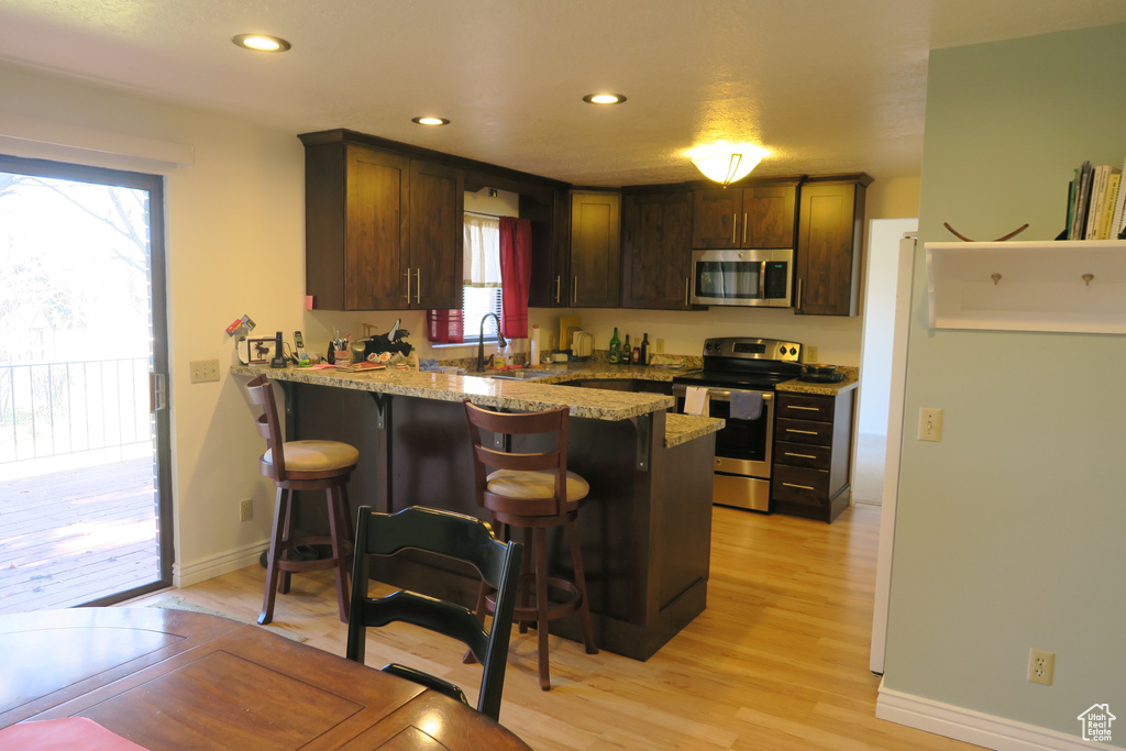 Kitchen featuring stainless steel appliances, a peninsula, a kitchen breakfast bar, light wood finished floors, and light stone countertops