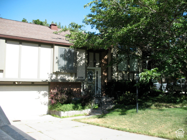 View of front facade with brick siding, driveway, a front lawn, a chimney, and a garage