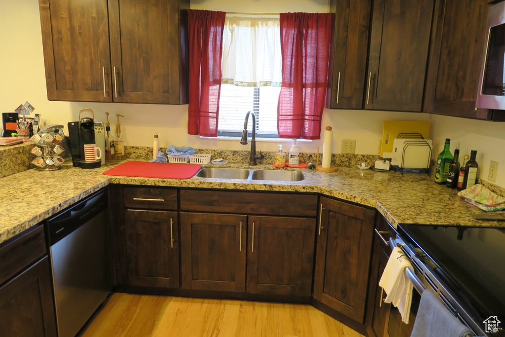 Kitchen featuring a sink, appliances with stainless steel finishes, light wood-style floors, and light stone counters