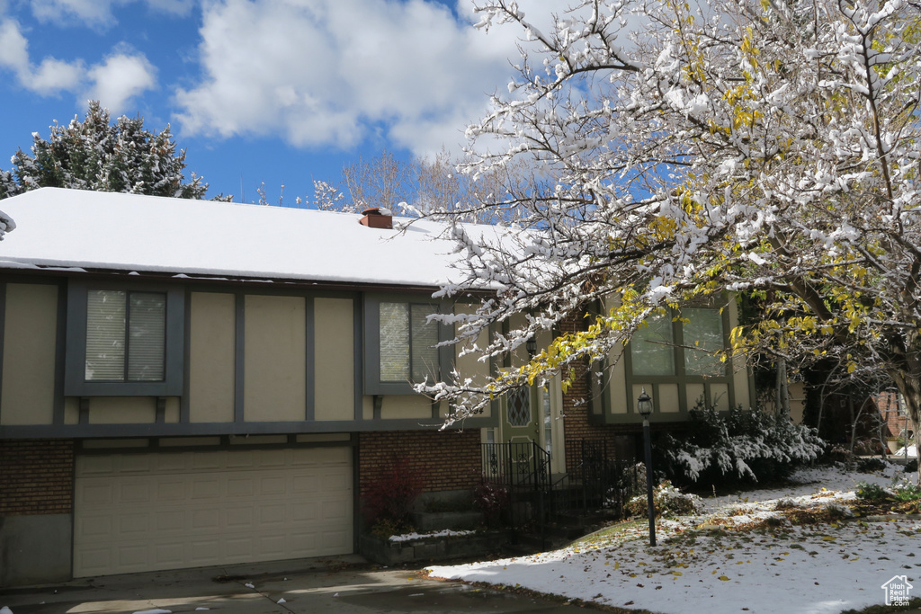 View of front of house with brick siding, a garage, a chimney, and driveway