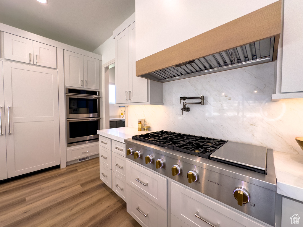 Kitchen featuring custom range hood, appliances with stainless steel finishes, light countertops, backsplash, and white cabinetry
