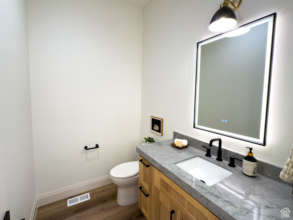Half bath with toilet, vanity, baseboards, and wood finished floors