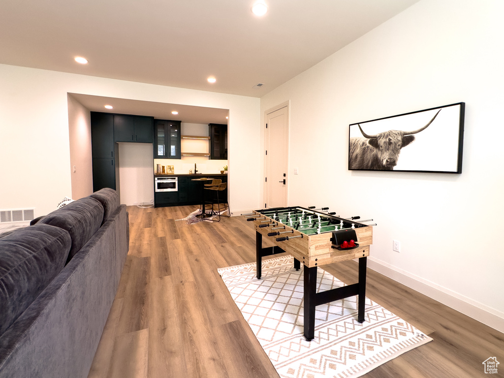 Rec room with bar with sink, light wood-style floors, recessed lighting, and baseboards