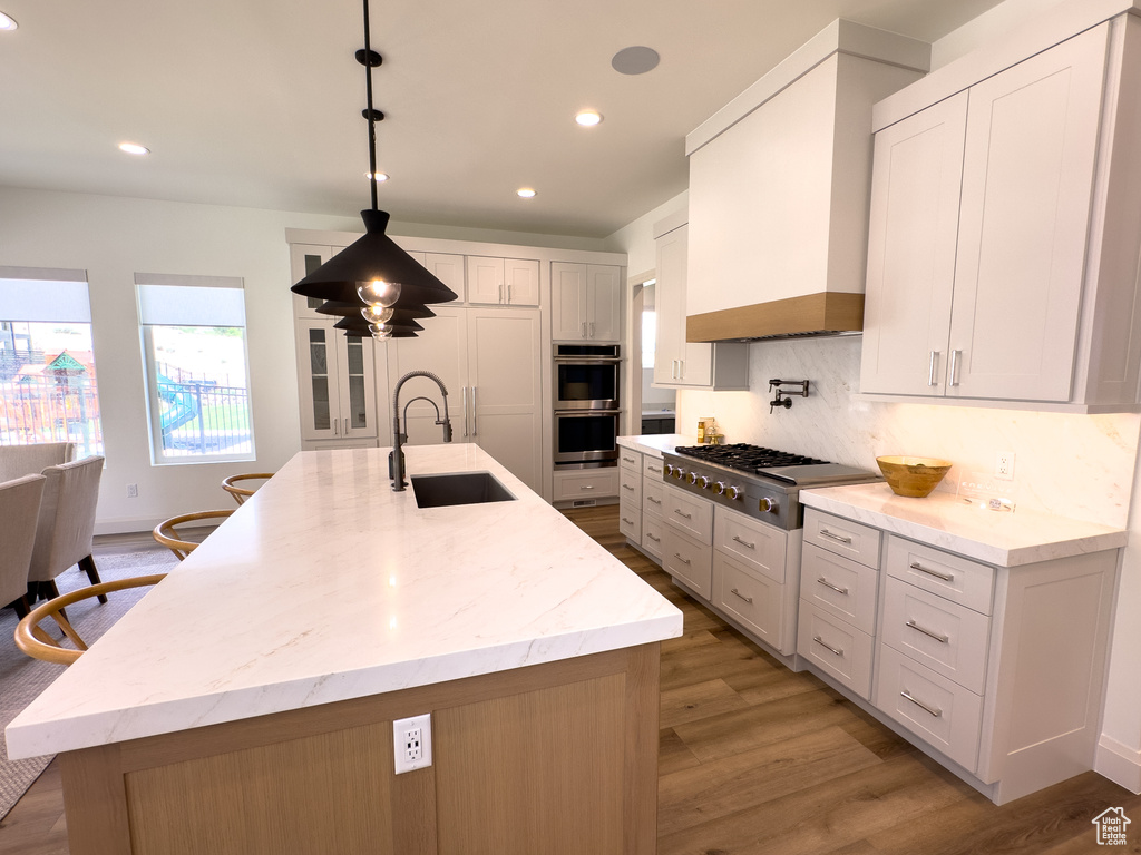 Kitchen with appliances with stainless steel finishes, a sink, light wood-style floors, recessed lighting, and premium range hood