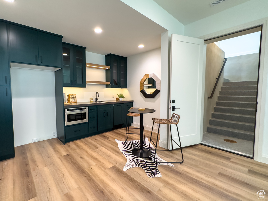 Kitchen with oven, light wood-style flooring, glass insert cabinets, recessed lighting, and a sink