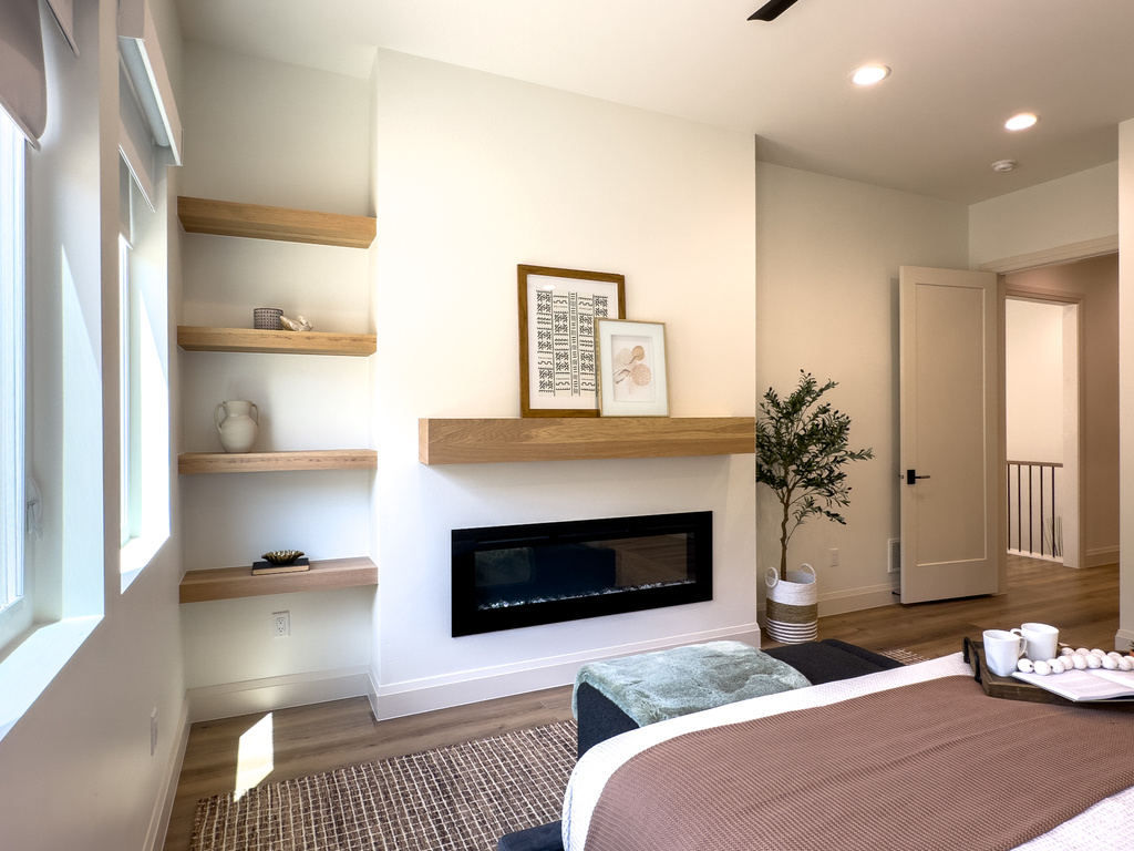 Bedroom with a glass covered fireplace, wood finished floors, recessed lighting, and baseboards