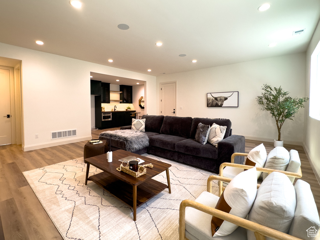 Living room with recessed lighting, light wood-style flooring, baseboards, and bar