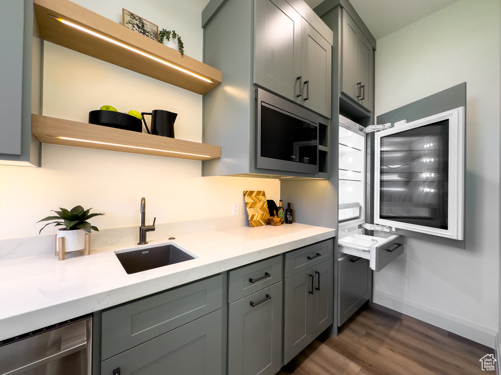 Kitchen featuring open shelves, a sink, stainless steel microwave, gray cabinetry, and dark wood-type flooring