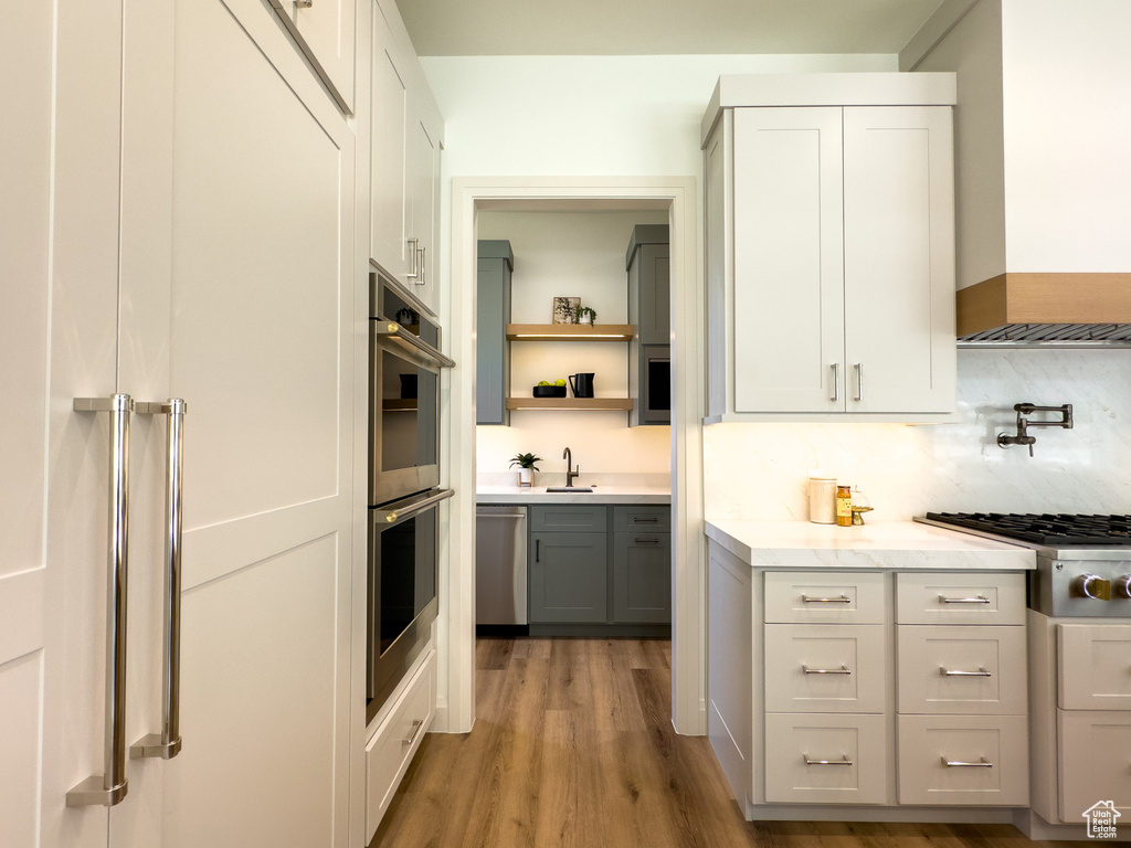 Kitchen featuring stainless steel appliances, wood finished floors, premium range hood, light stone countertops, and open shelves