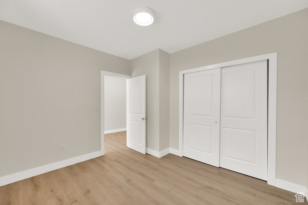Unfurnished bedroom with light wood-style floors, baseboards, and a closet