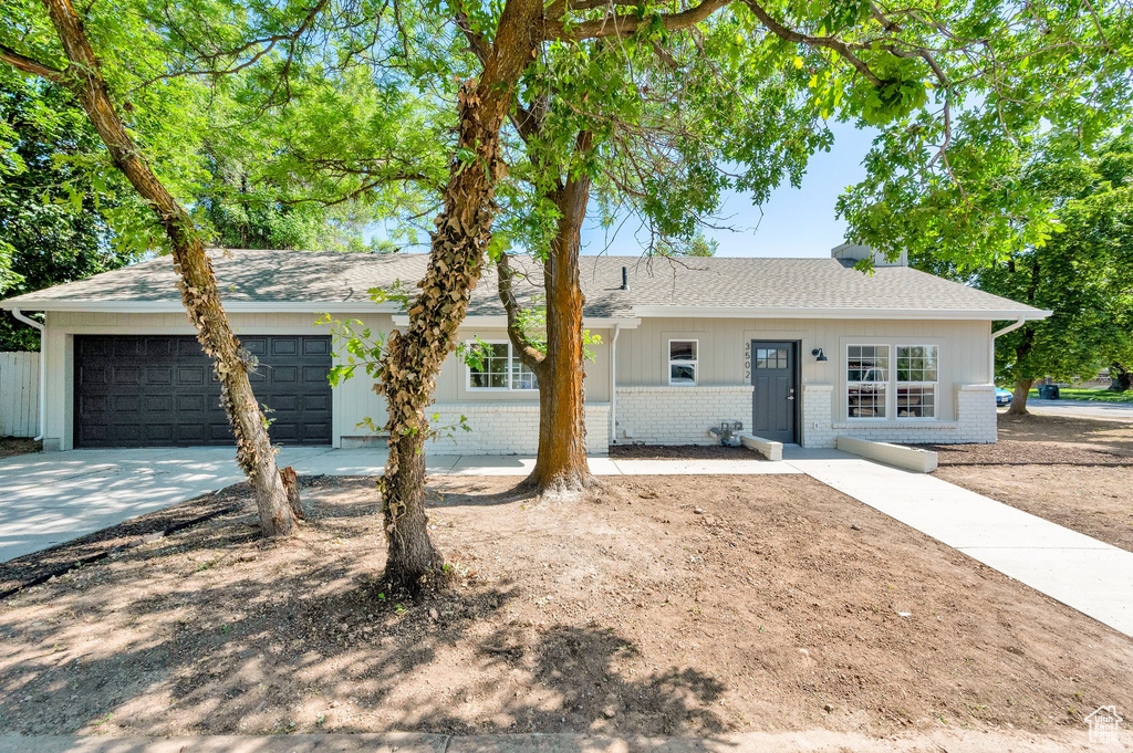 Ranch-style house featuring brick siding, an attached garage, driveway, and roof with shingles