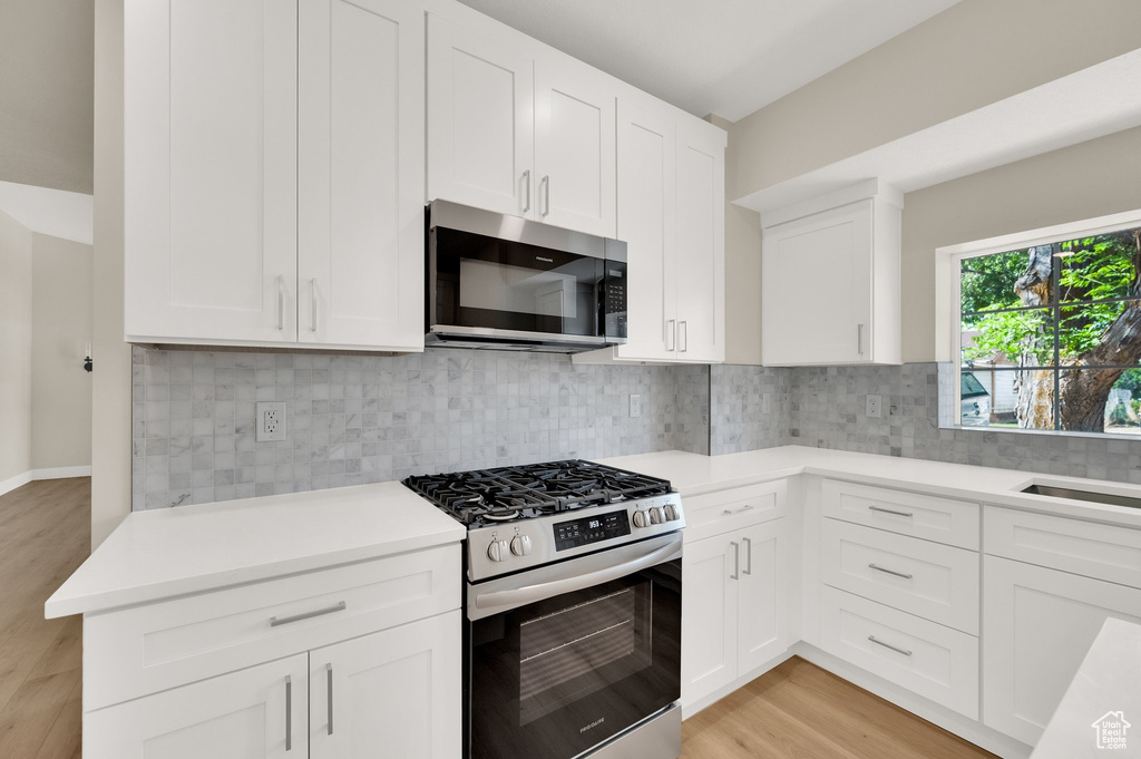 Kitchen with stainless steel appliances, light wood-style flooring, light countertops, white cabinetry, and backsplash