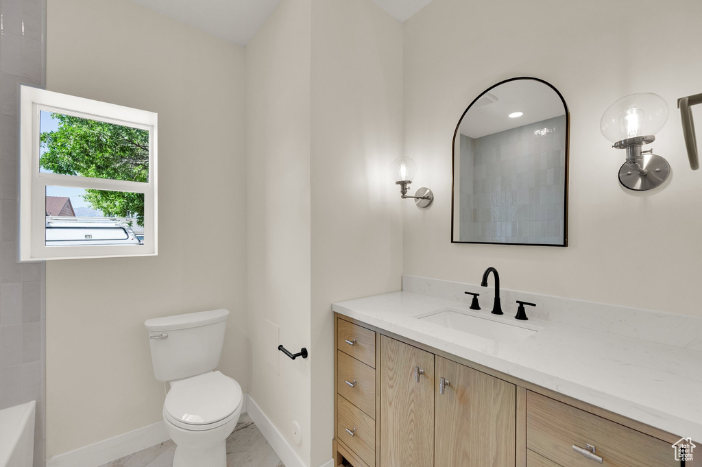Full bathroom with vanity, toilet, baseboards, a tub to relax in, and marble look tiles