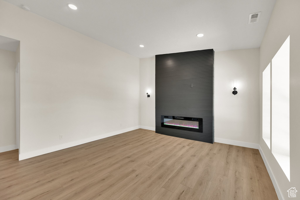 Unfurnished living room featuring light wood-style floors, baseboards, a fireplace, and recessed lighting