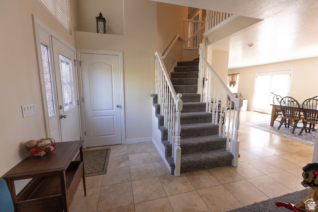 Foyer entrance featuring stairway, light tile patterned flooring, a high ceiling, and baseboards