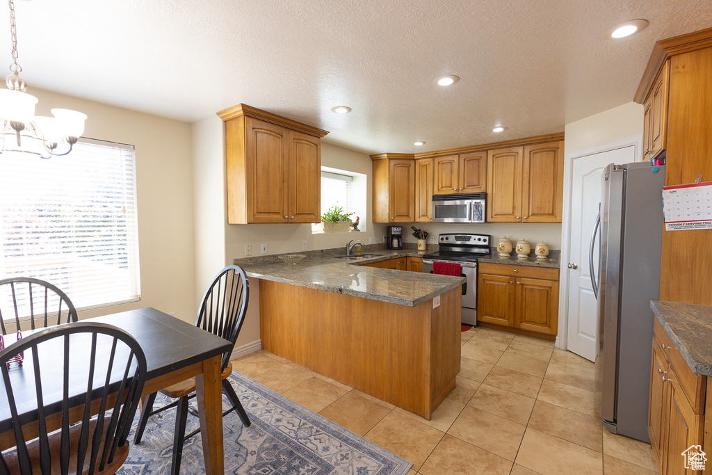 Kitchen with stainless steel appliances, a peninsula, a chandelier, brown cabinets, and recessed lighting