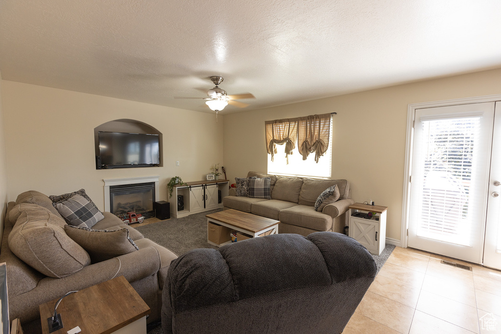 Living area featuring ceiling fan, a glass covered fireplace, light tile patterned flooring, and baseboards