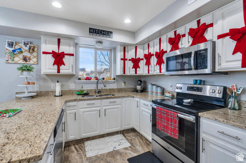 Kitchen featuring stainless steel appliances, a sink, white cabinetry, recessed lighting, and light stone countertops