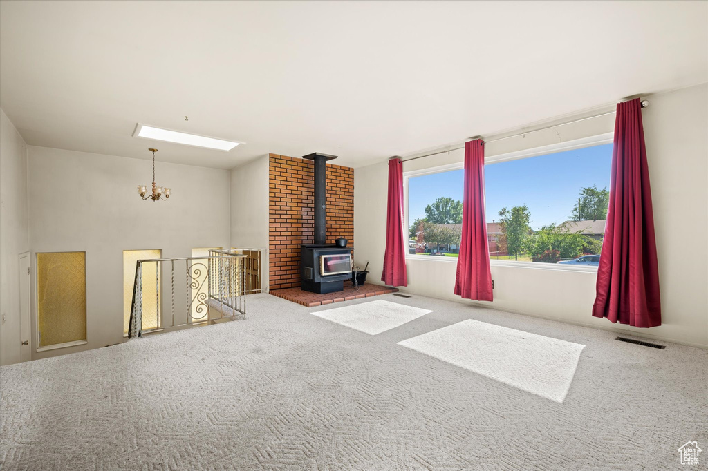 Unfurnished living room with a chandelier, carpet, a skylight, and a wood stove