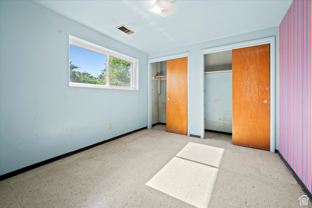 Unfurnished bedroom with tile patterned floors, two closets, and baseboards