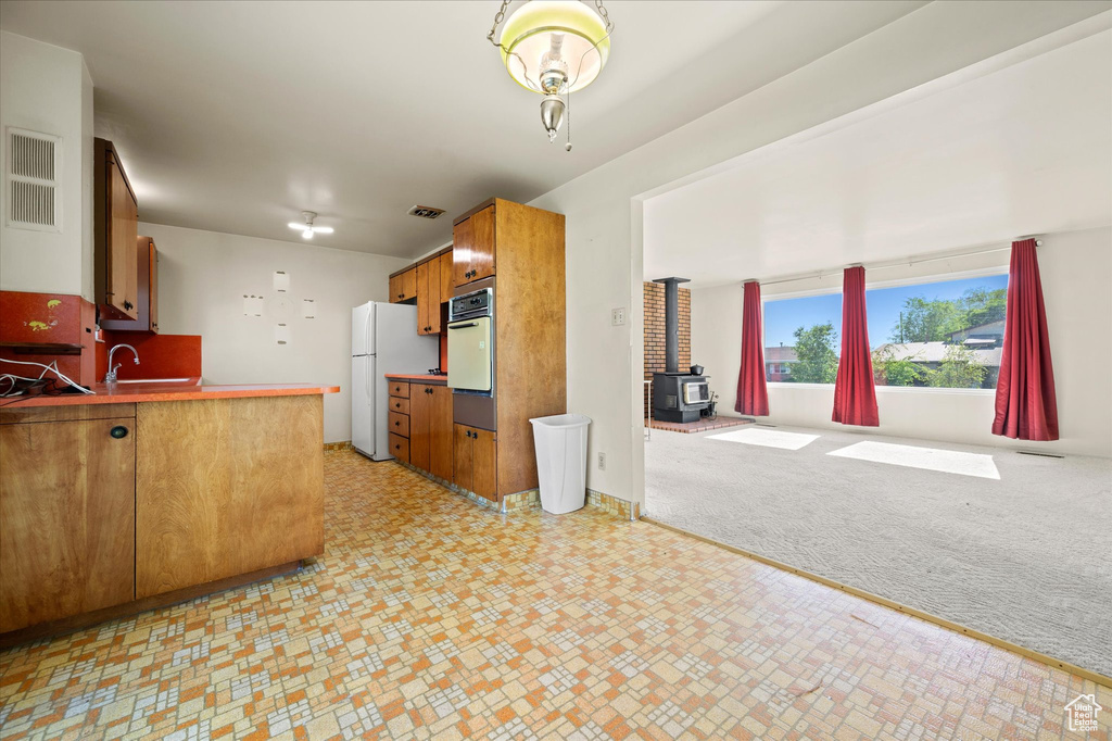 Kitchen featuring white appliances, a wood stove, brown cabinets, a sink, and open floor plan