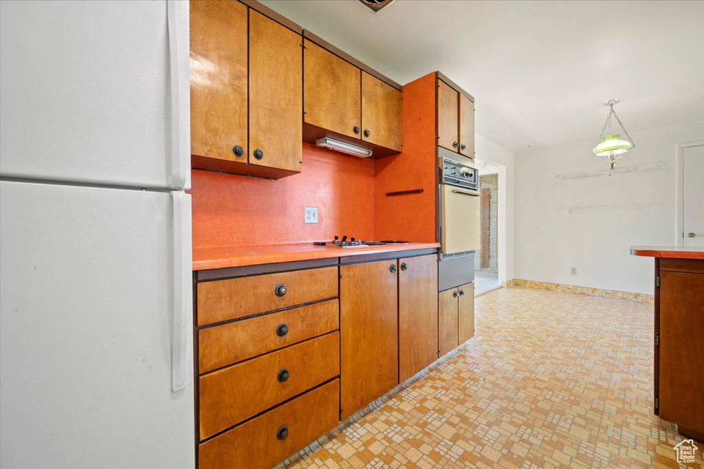 Kitchen with white appliances, brown cabinetry, light countertops, brick patterned flooring, and a warming drawer